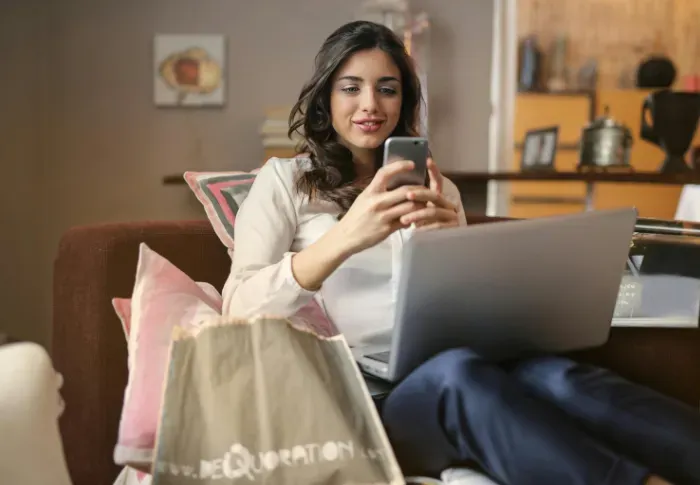 A woman shopping on her phone with a laptop on her lap