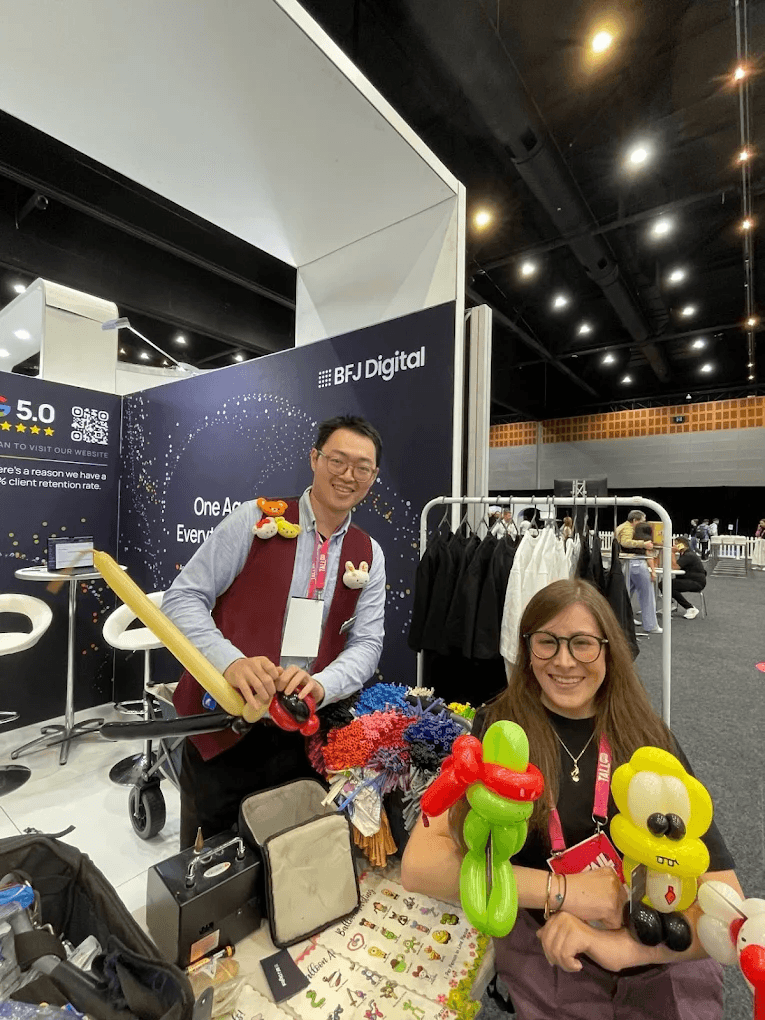 Two BFJ Digital team members at the agency’s expo stand, holding balloon animals in front of the BFJ Digital backdrop