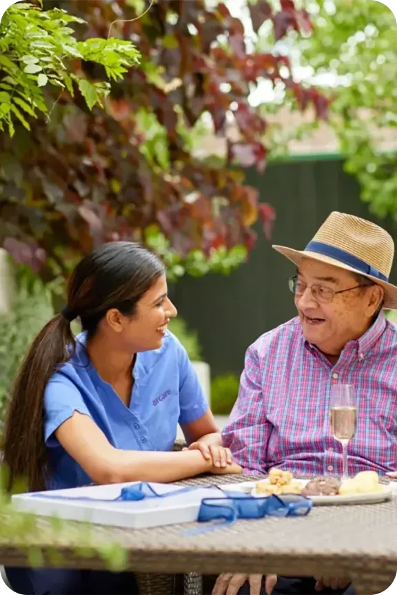 An aged care worker and an older man sharing a drink outdoors