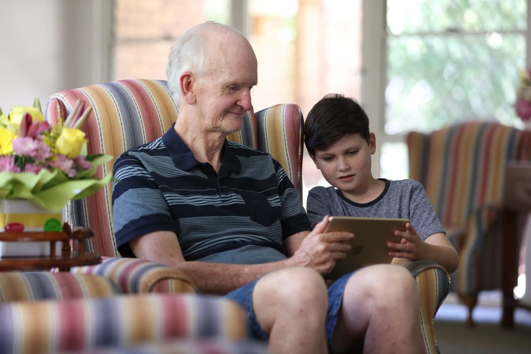 A young boy with his grandfather, both looking at a tablet device