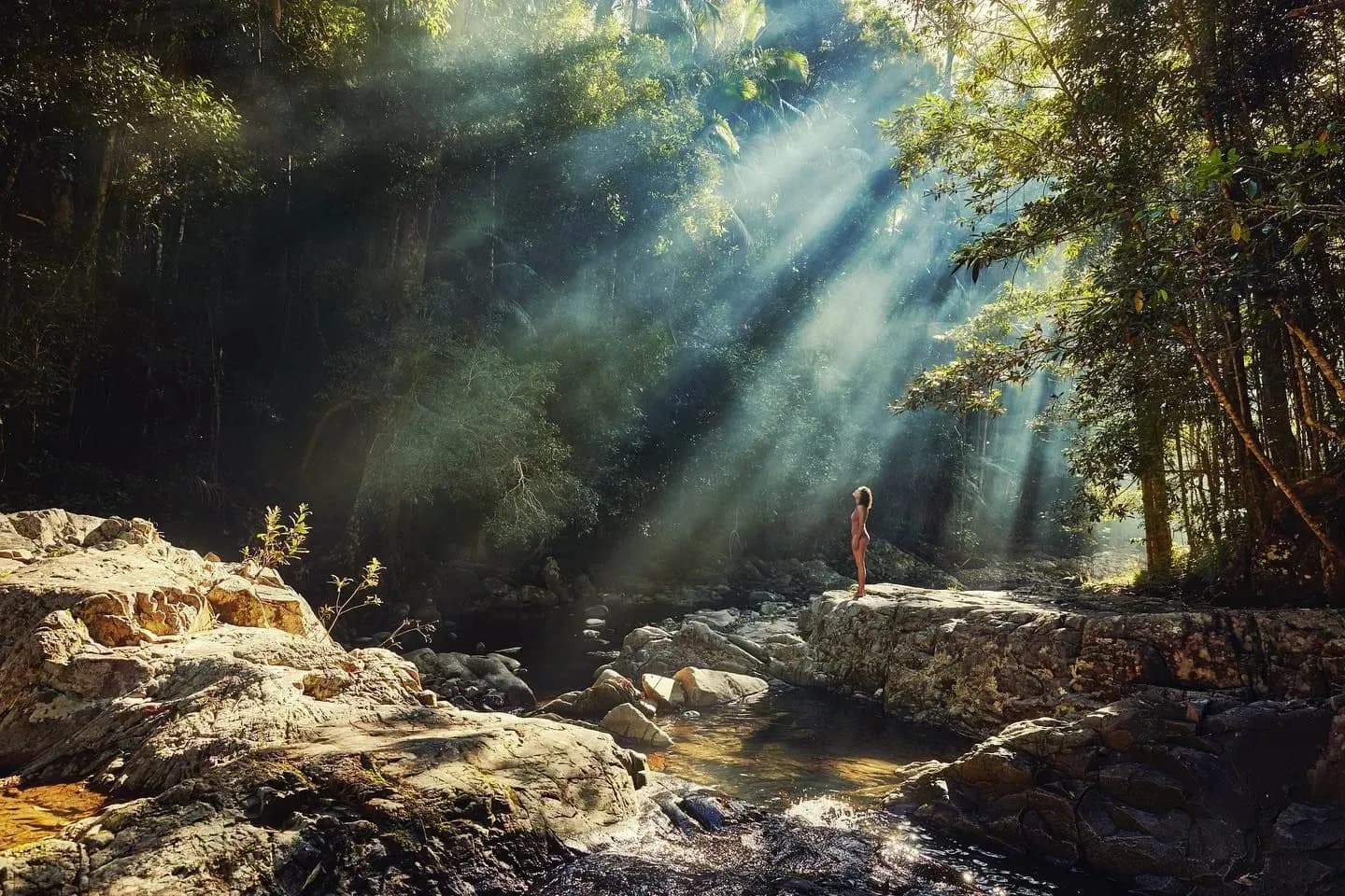 Josh Kelly photgraphy of a woman standing by a beautiful creek with sunlight shining through tree canopy